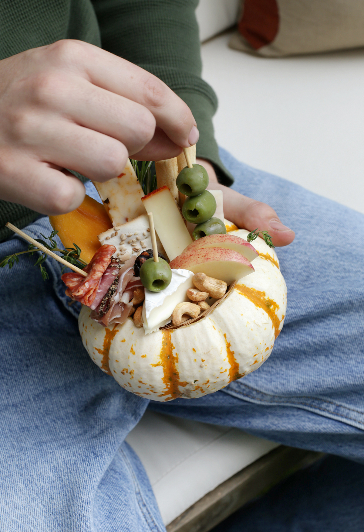 hand grabbing skewer of olives out of mini pumpkin charcuterie